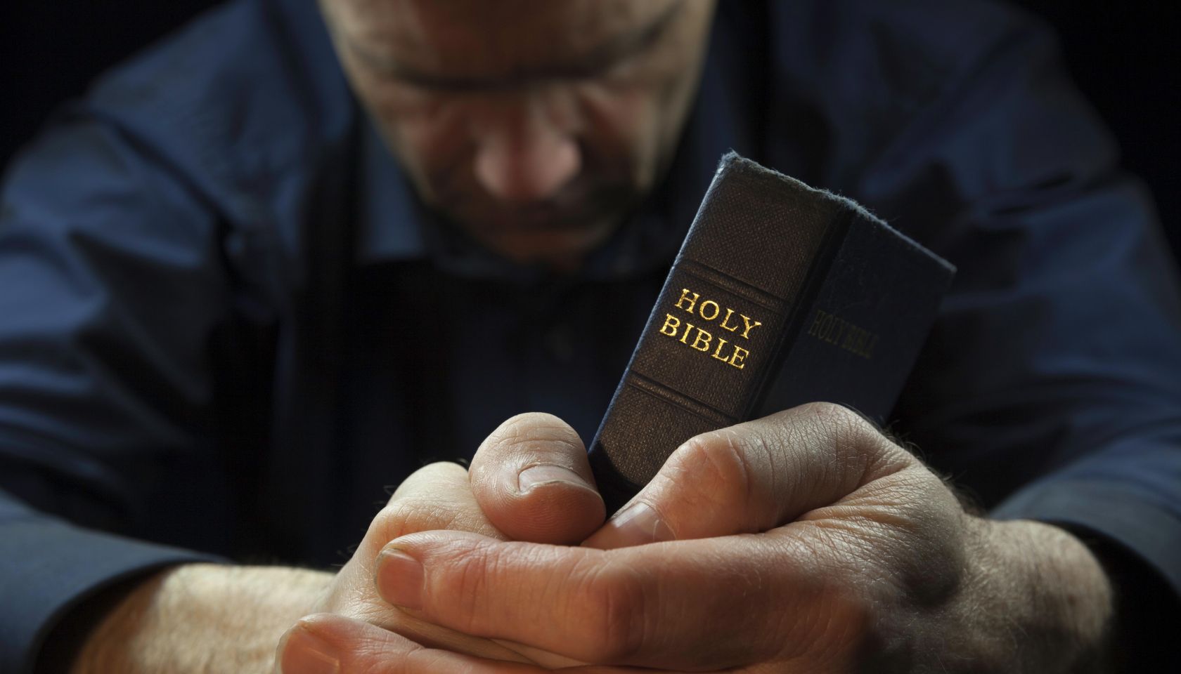 A Man praying holding a Holy Bible.