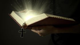 Hands of man holding holy bible and wooden rosary with magical rays