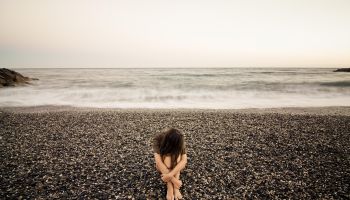 Young sad woman alone in a black stone beach.