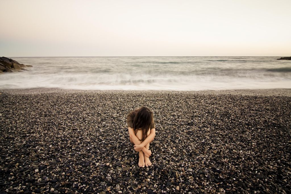 Young sad woman alone in a black stone beach.