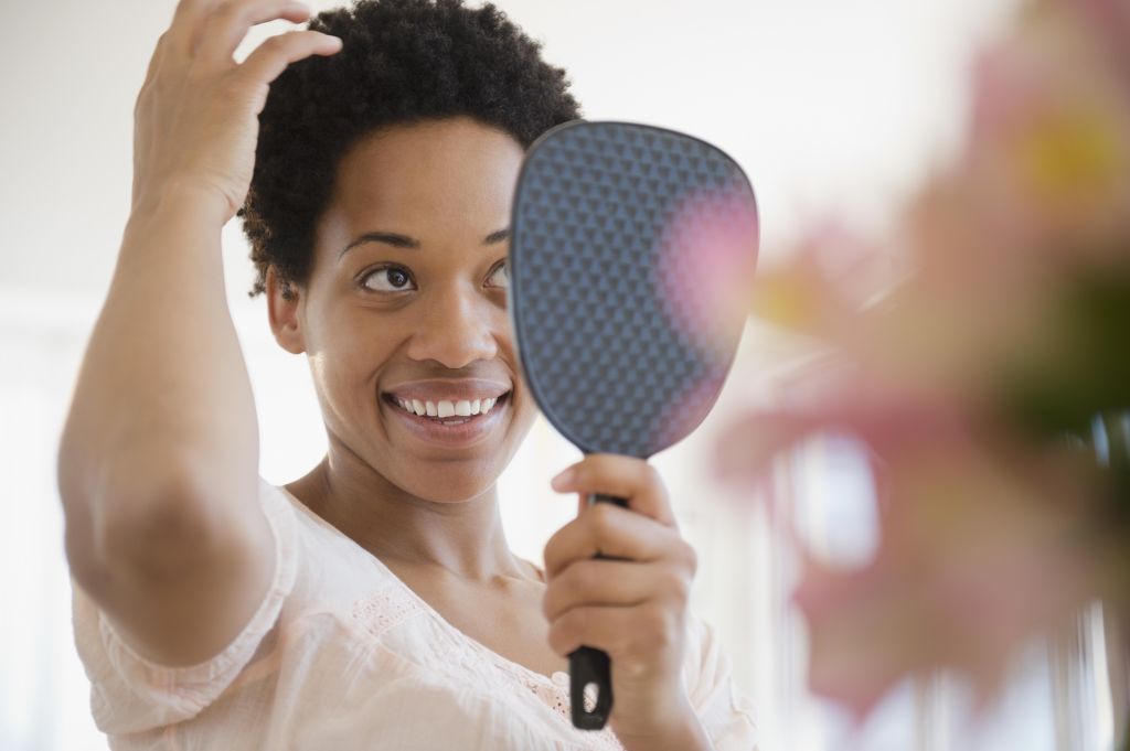 African American woman checking hair in mirror