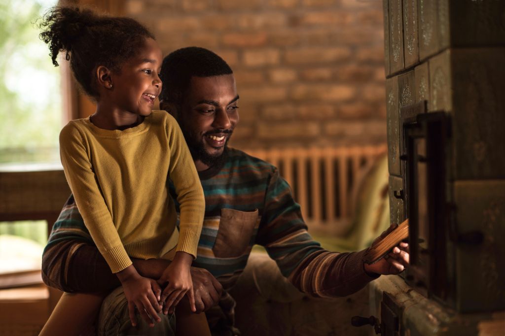 Happy father and daughter putting a wood into the fireplace.