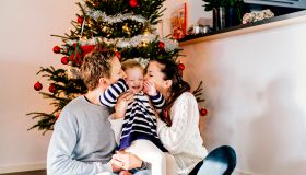 Parents kissing daughter while sitting against Christmas tree at home