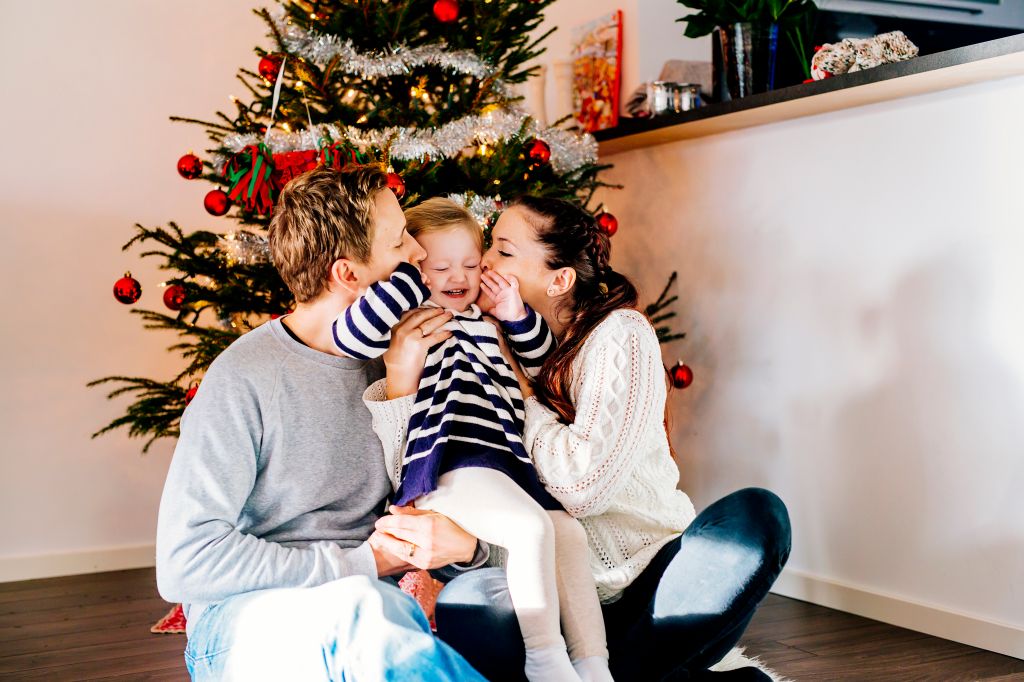 Parents kissing daughter while sitting against Christmas tree at home