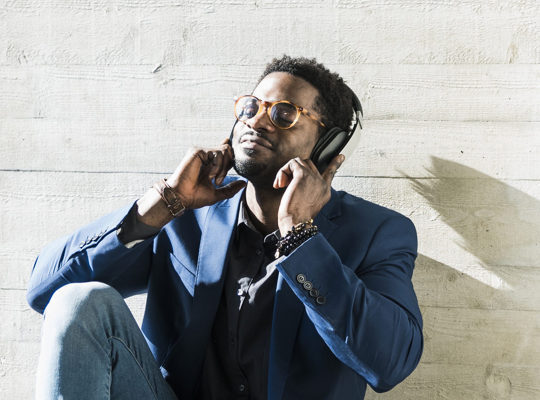 Businessman sitting on the floor in sunshine wearing headphones