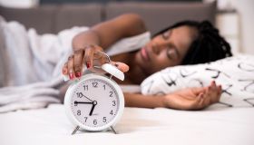 Tired woman switching off her alarm clock in her bedroom