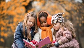 Three small girls reading a children's book in autumn day.