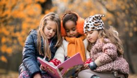 Three small girls reading a children's book in autumn day.