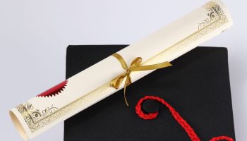 High Angle View Of Mortarboard And Diploma On White Background