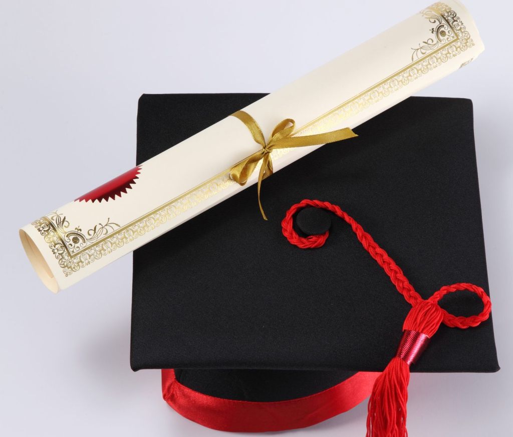 High Angle View Of Mortarboard And Diploma On White Background