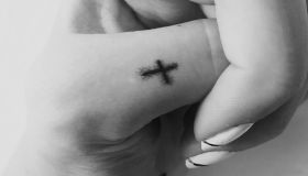 Cropped Hand Of Woman Showing Cross Tattoo Against Wall