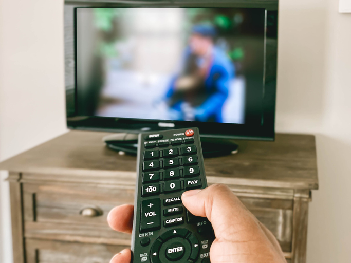 Close-Up View of Hand Pointing Remote Control at TV