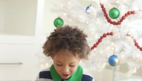 Young boy sitting under Christmas tree, opening Christmas presents