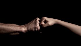 two hands fist bump together over black background