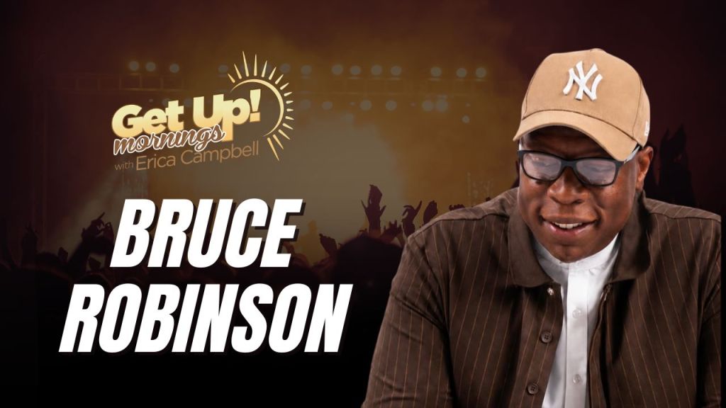 A smiling man wearing a New York Yankees baseball cap and glasses, standing in front of a "Get Up! Mornings with Erica Campbell" backdrop.
