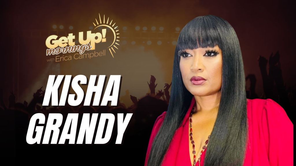 A woman with long black hair wearing a red top stands in front of a backdrop with the text "Get Up! mornings with Erica Campbell" and "KISHA GRANDY".
