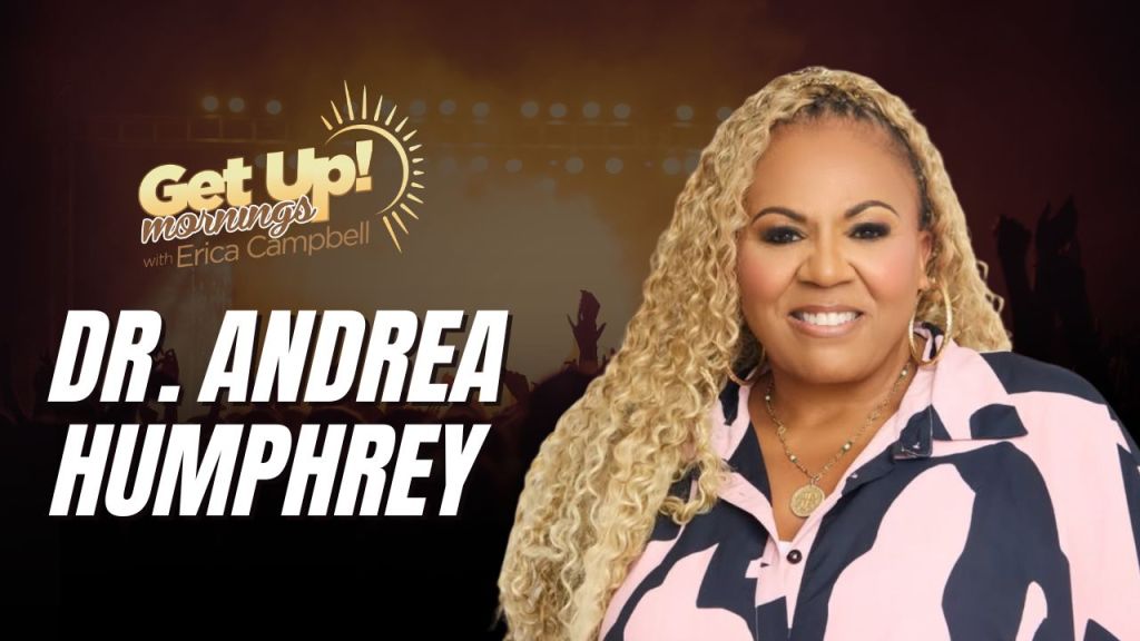 A smiling woman with curly blonde hair wearing a pink and black patterned jacket, standing in front of a "Get Up! Mornings with Erica Campbell" backdrop.