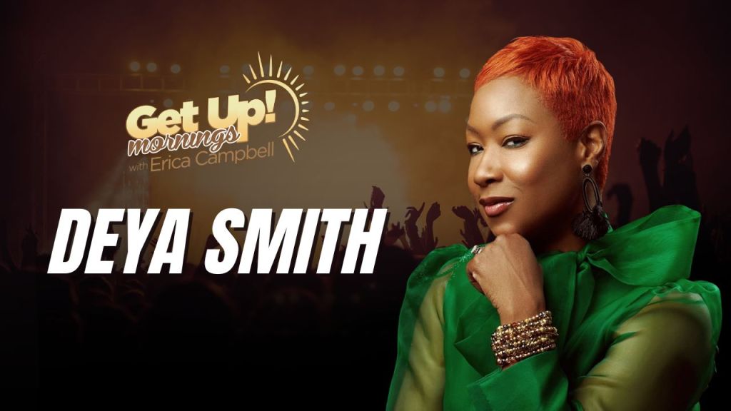 A woman with short red hair wearing a green dress and jewelry stands in front of a "Get Up! Mornings with Erica Campbell" backdrop.