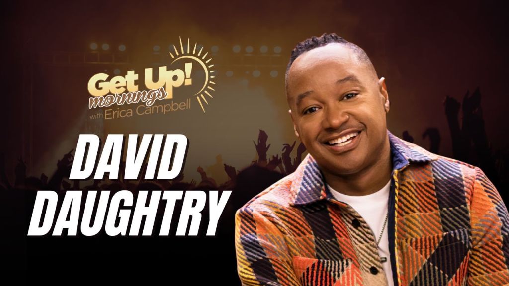 A smiling man wearing a colorful patterned jacket stands in front of a "Get Up! Mornings with Erica Campbell" backdrop with the text "DAVID DAUGHTRY".